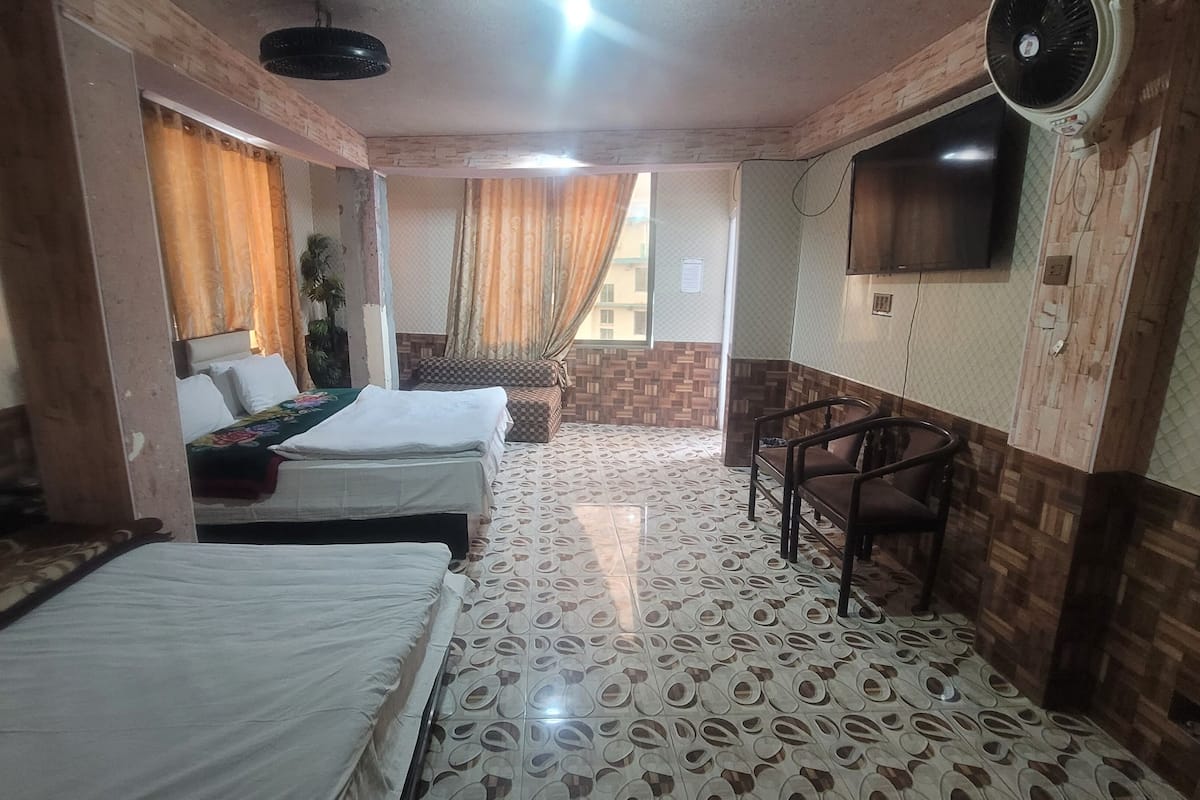 A hotel room with two beds, a small seating area, a TV mounted on the wall, and patterned flooring.
