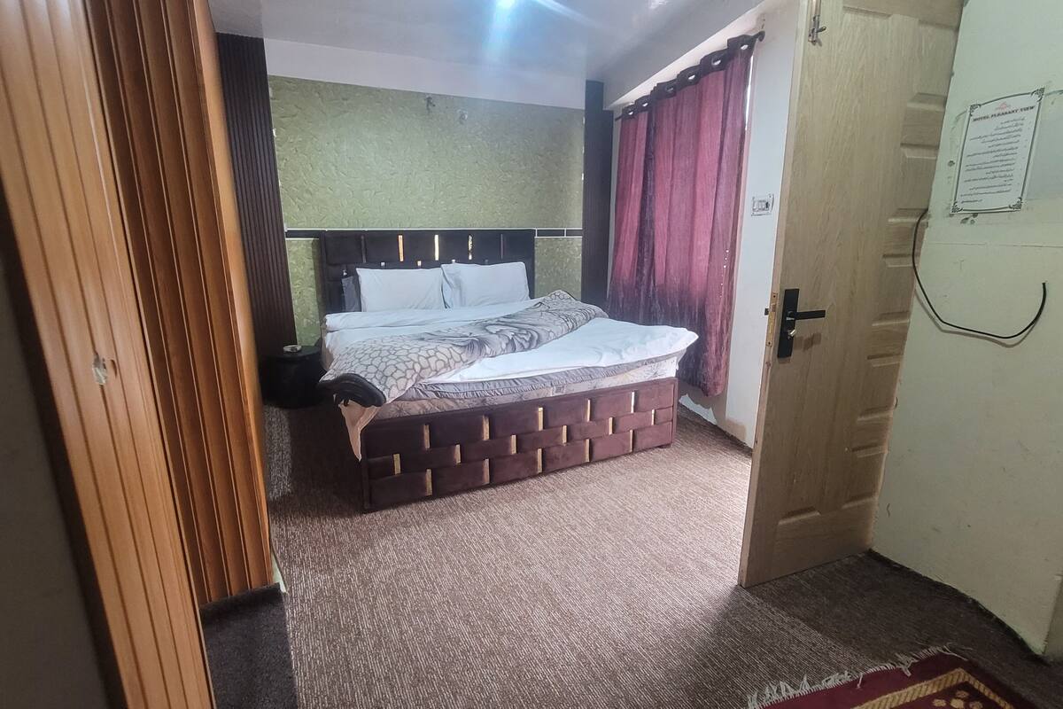 A bedroom with a bed, a nightstand, a wooden door, and a wall-mounted light fixture.
