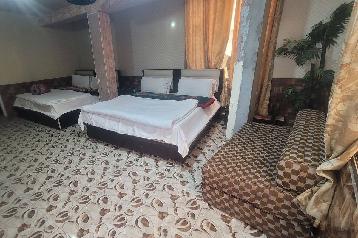 A hotel room with two beds, patterned floor tiles, and a checkered sofa.