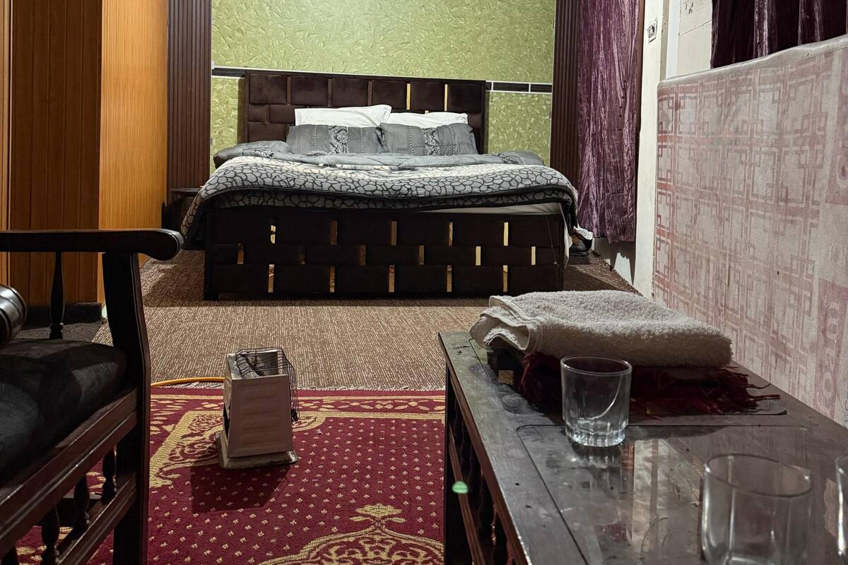 A hotel room with a bed, a wooden chair, a small table with a glass, and a patterned carpet.