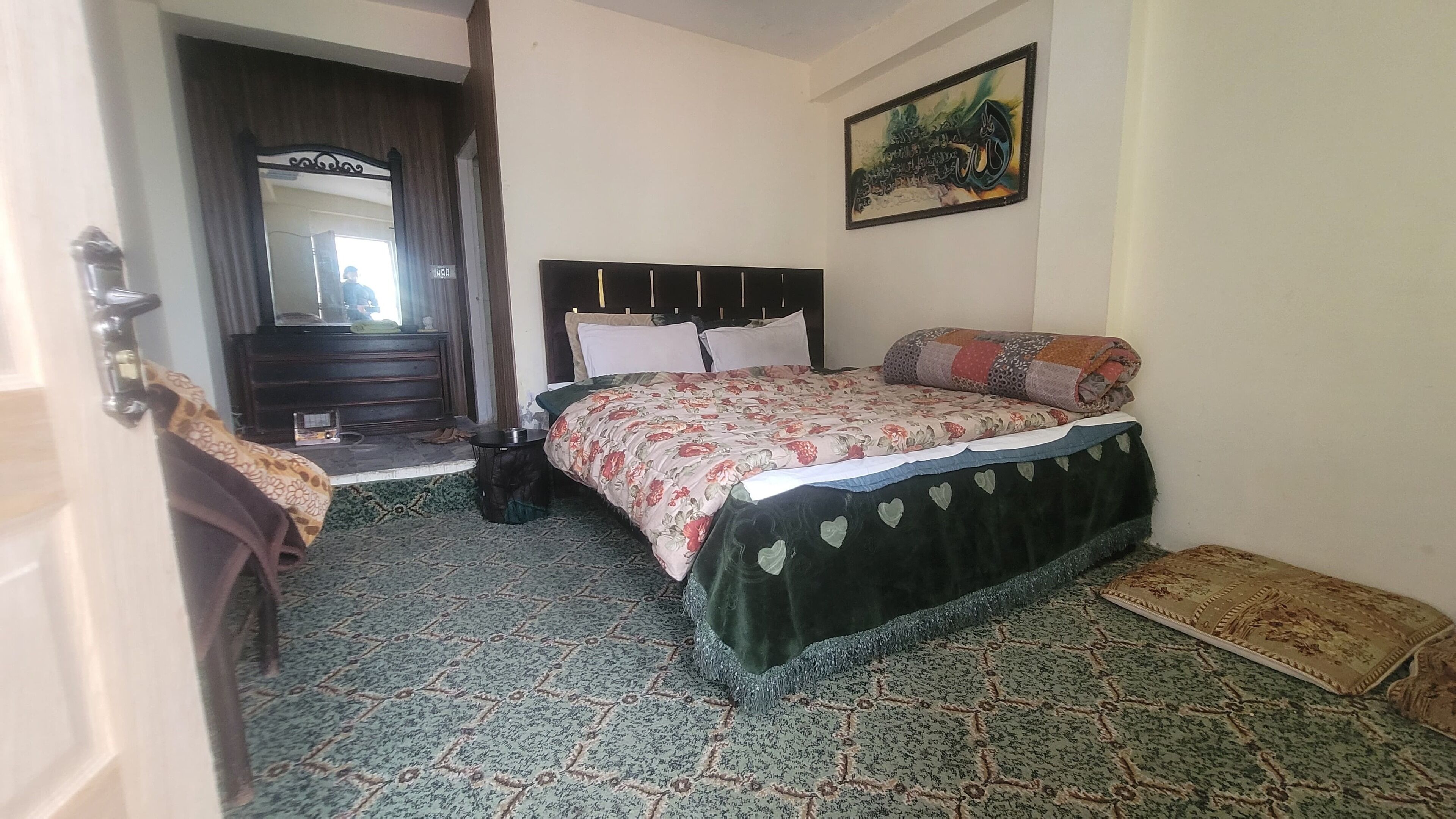 A bedroom with a bed, a dresser, a mirror, and a painting on the wall.