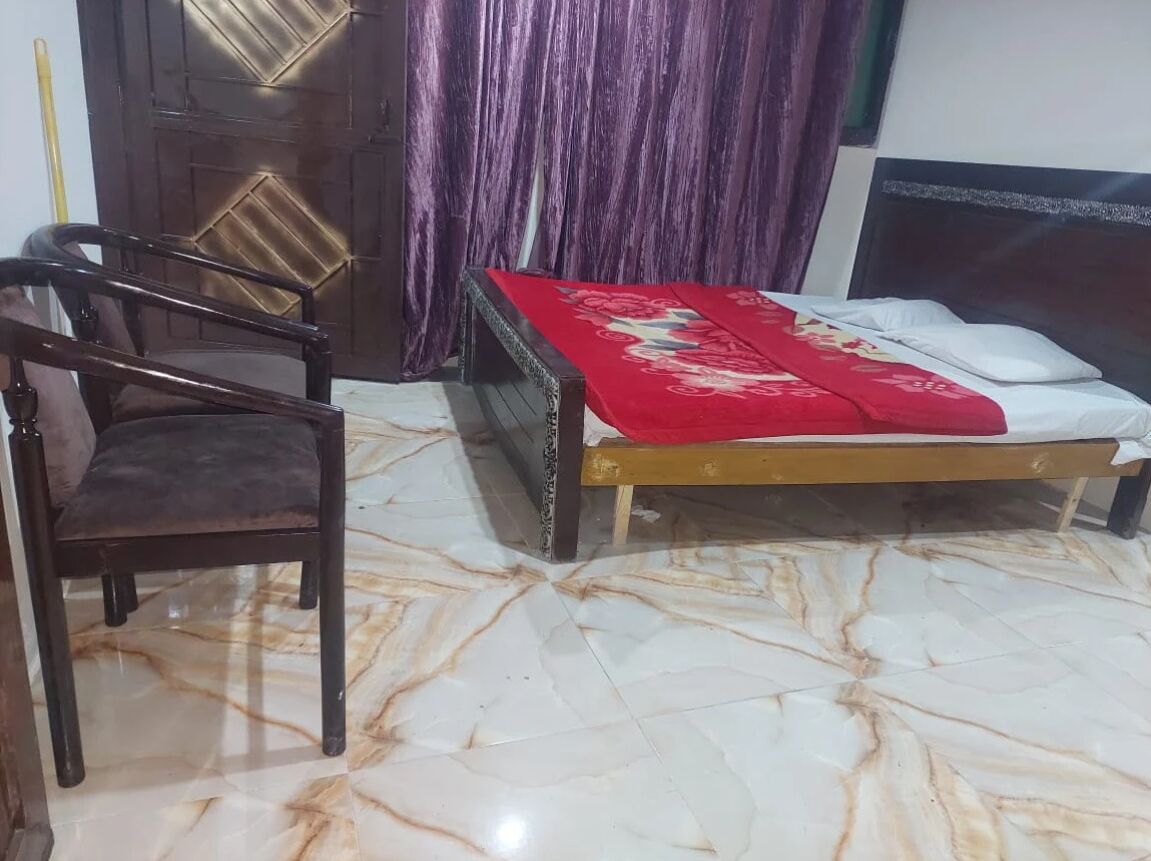 A room with a bed, a chair, a wooden door, and a curtain.