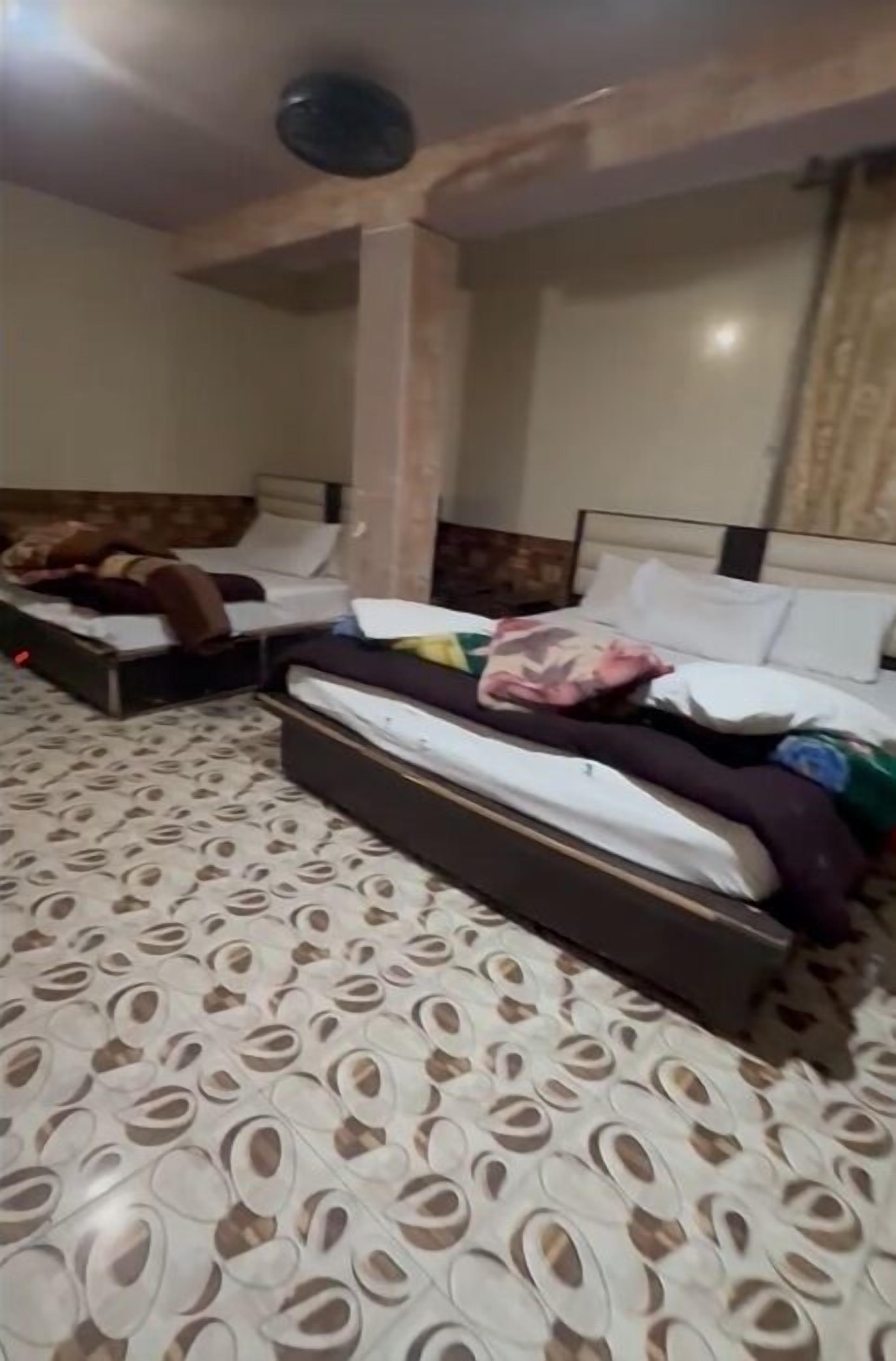 Une chambre d’hôtel avec deux lits, des carreaux de sol à motifs et un ventilateur de plafond.