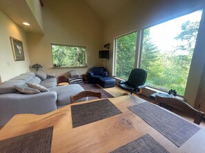 A living room with a sofa, a dining table, and a large window with a view of trees. - Beautiful, peaceful mountain view cabin. (Arlington)