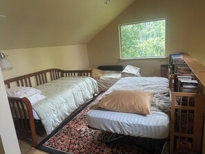 A bedroom with two single beds, a window with a view of greenery, and a bookshelf with books. - Beautiful, peaceful mountain view cabin. (Arlington)