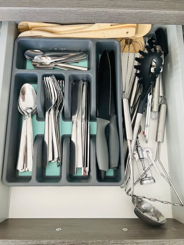 A drawer with compartments containing various kitchen utensils such as spoons, forks, knives, and a grater.