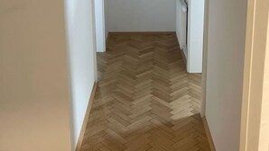 A narrow hallway with a herringbone wooden floor, white walls, and a ceiling light.