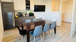 A modern kitchen with a dining area, wooden flooring, and a flat-screen TV.