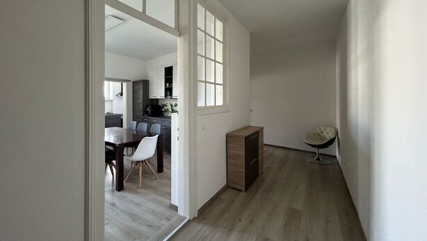 A hallway with a wooden floor leading to a dining area with a table and chairs.
