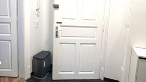 A hallway with a white door, a trash bin, and a small cabinet. - Apartment Graz Eggenberg Top 8 (Graz)