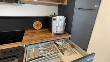 Una cocina con encimera de madera, cafetera y un cajón con utensilios.