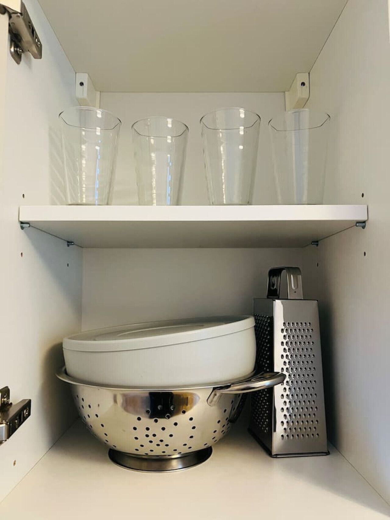 A kitchen with a white shelf holding three clear glasses, a colander, and a grater.