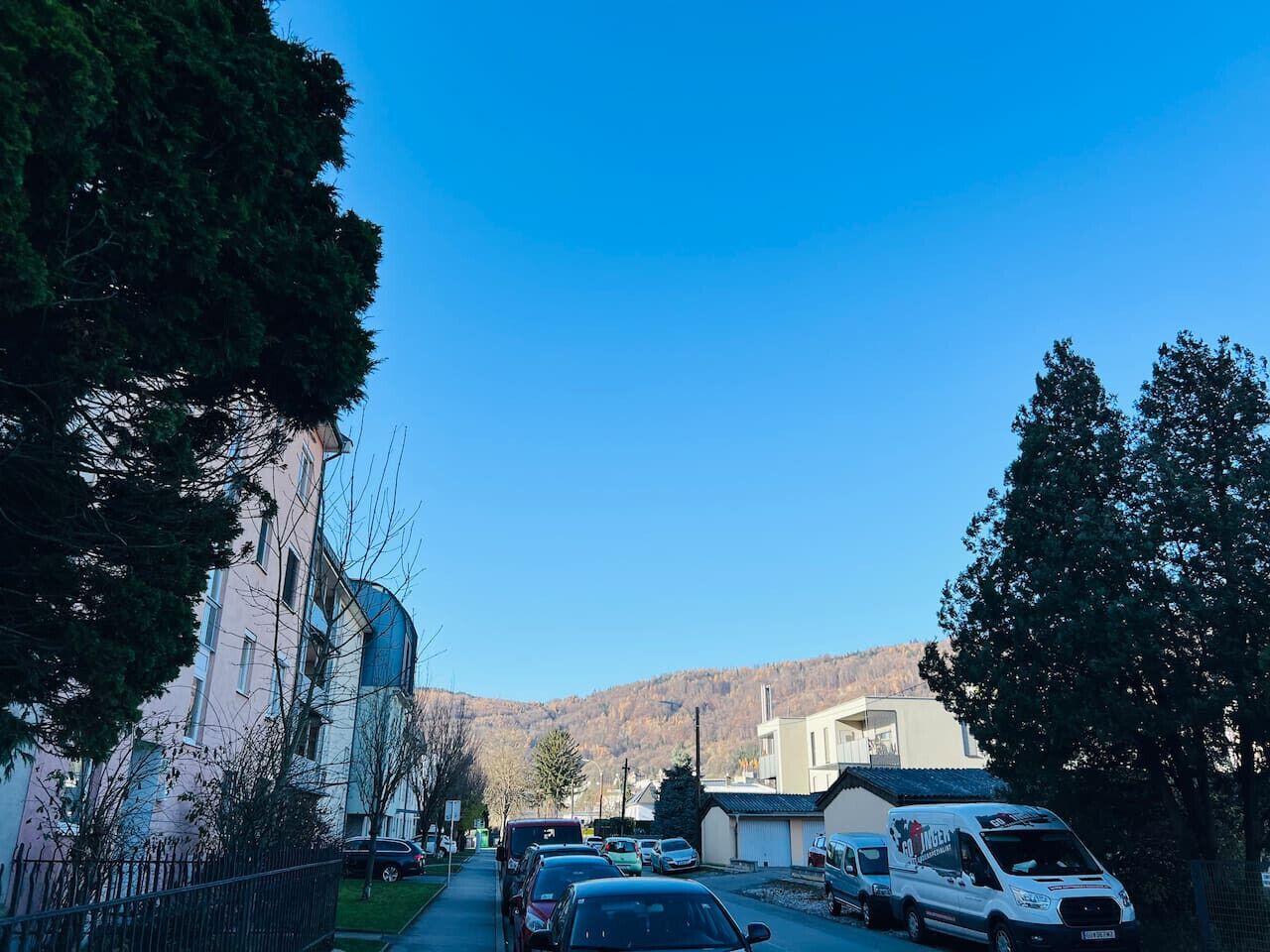 A street view with parked cars, a building with a dome, and a mountain in the background.