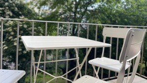 A white metal table and chair set on a balcony with a metal railing, surrounded by greenery. - 123 Apartment Graz - top 1 (Graz)