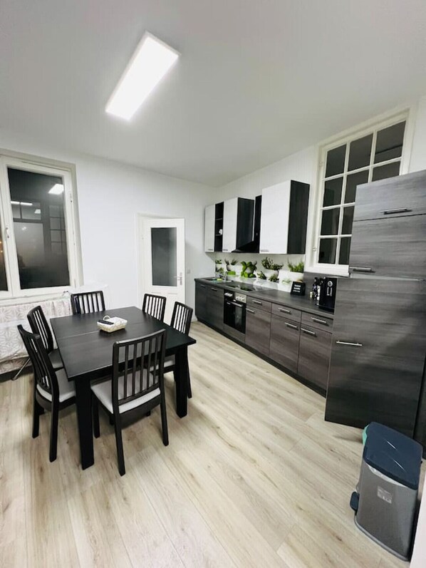 Une cuisine moderne avec une table à manger, des chaises, des placards, un réfrigérateur et une fenêtre.