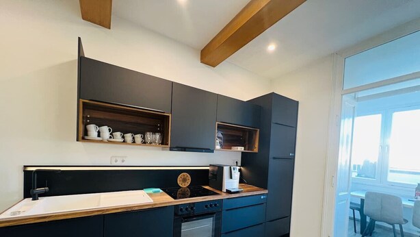 A modern kitchen with dark cabinetry, a wooden countertop, and a built-in oven. - Perfect for large travel groups! Leoben! (Leitendorf)