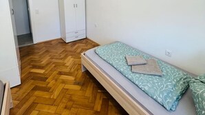 A small, sparsely furnished room with a wooden herringbone floor, a single bed with patterned bedding, and a white wardrobe. - Perfect for large travel groups! Leoben! (Leitendorf)