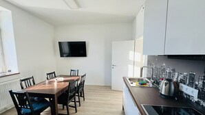 A modern kitchen with a cityscape backsplash, a dining area with a wooden table and chairs, and a flat-screen TV mounted on the wall. - Living Villa Rebuli! Top 5 (Leitendorf)
