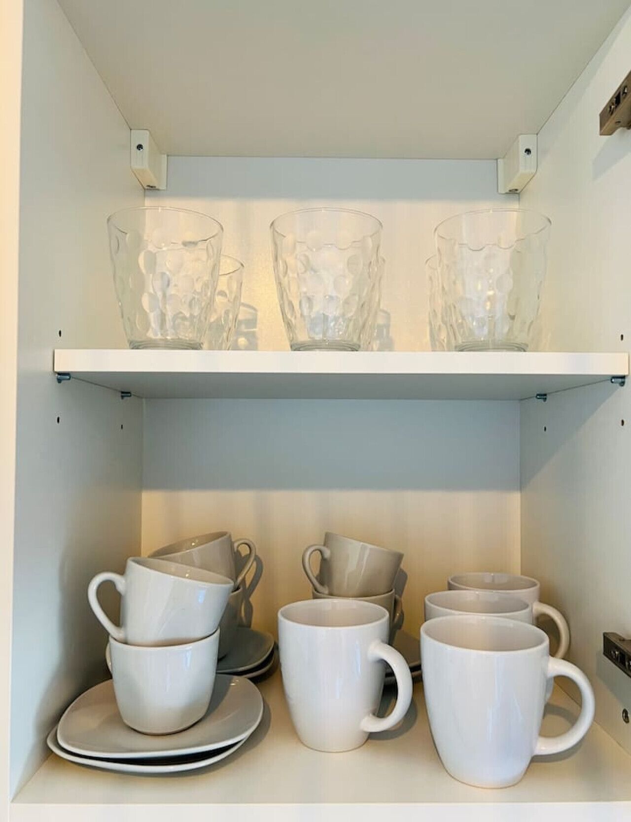 Une étagère avec des verres en verre transparent et des tasses en céramique blanche.
