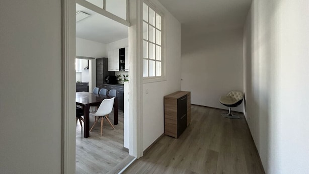 Un couloir doté d’un plancher en bois mène à une salle à manger où se trouvent une table et des chaises.