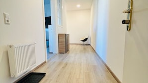 Un couloir étroit doté d’un plancher en bois, de murs blancs et d’une porte avec une poignée dorée.