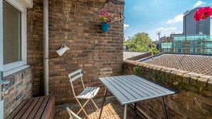 Ein Balkon mit Backsteinmauer, einem Metalltisch, einem Klappstuhl, einem Blumentopf und einer Hängelampe.