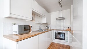 Eine moderne Küche mit weißen Schränken, einer Holz Arbeitsplatte, einem Einbauofen, einer Mikrowelle und einer Edelstahl-Dunstabzugshaube.