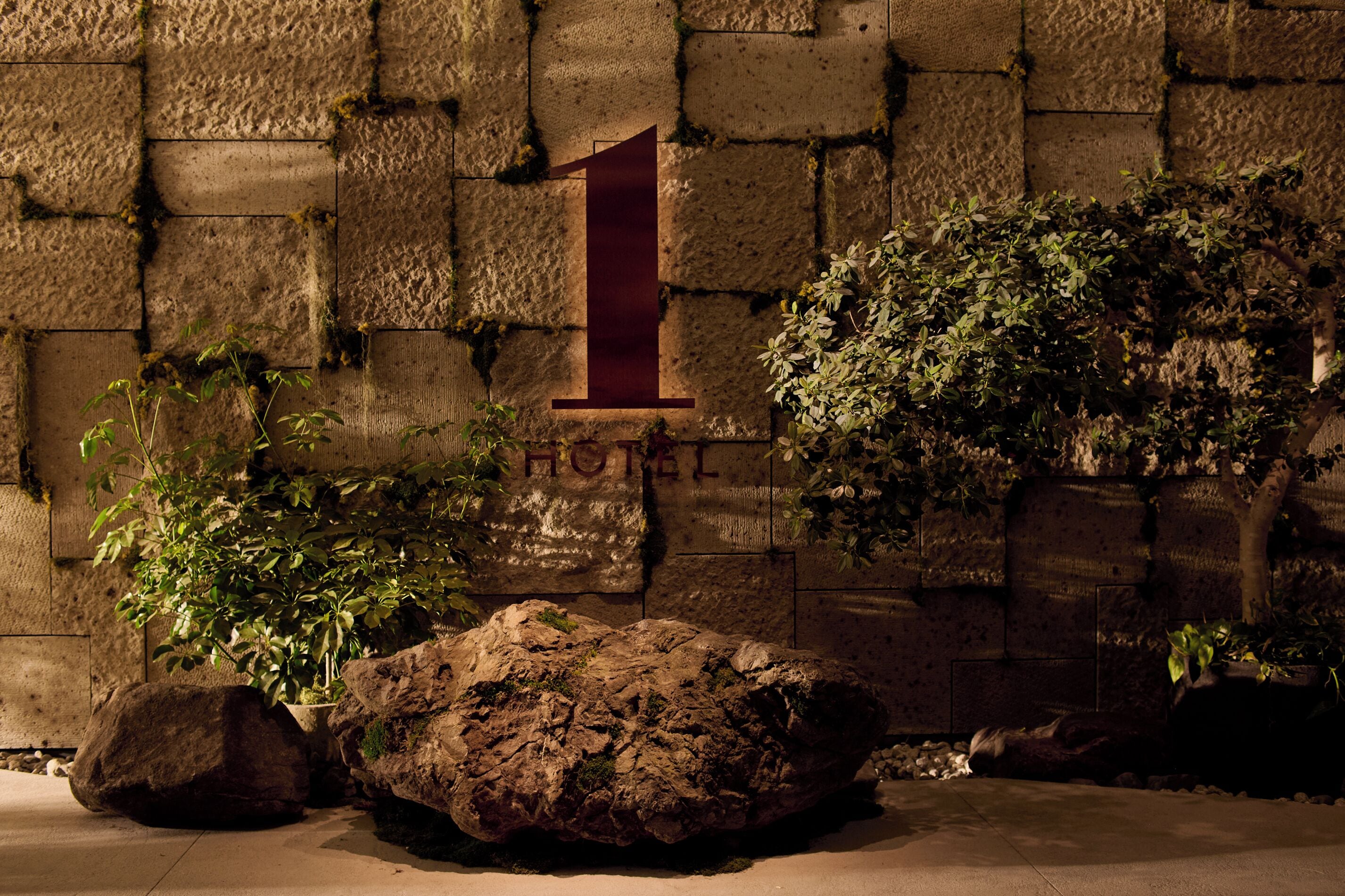 A stone wall with a large rock, a potted plant, and a sign with the number '1' and the word 'HOTEL'.