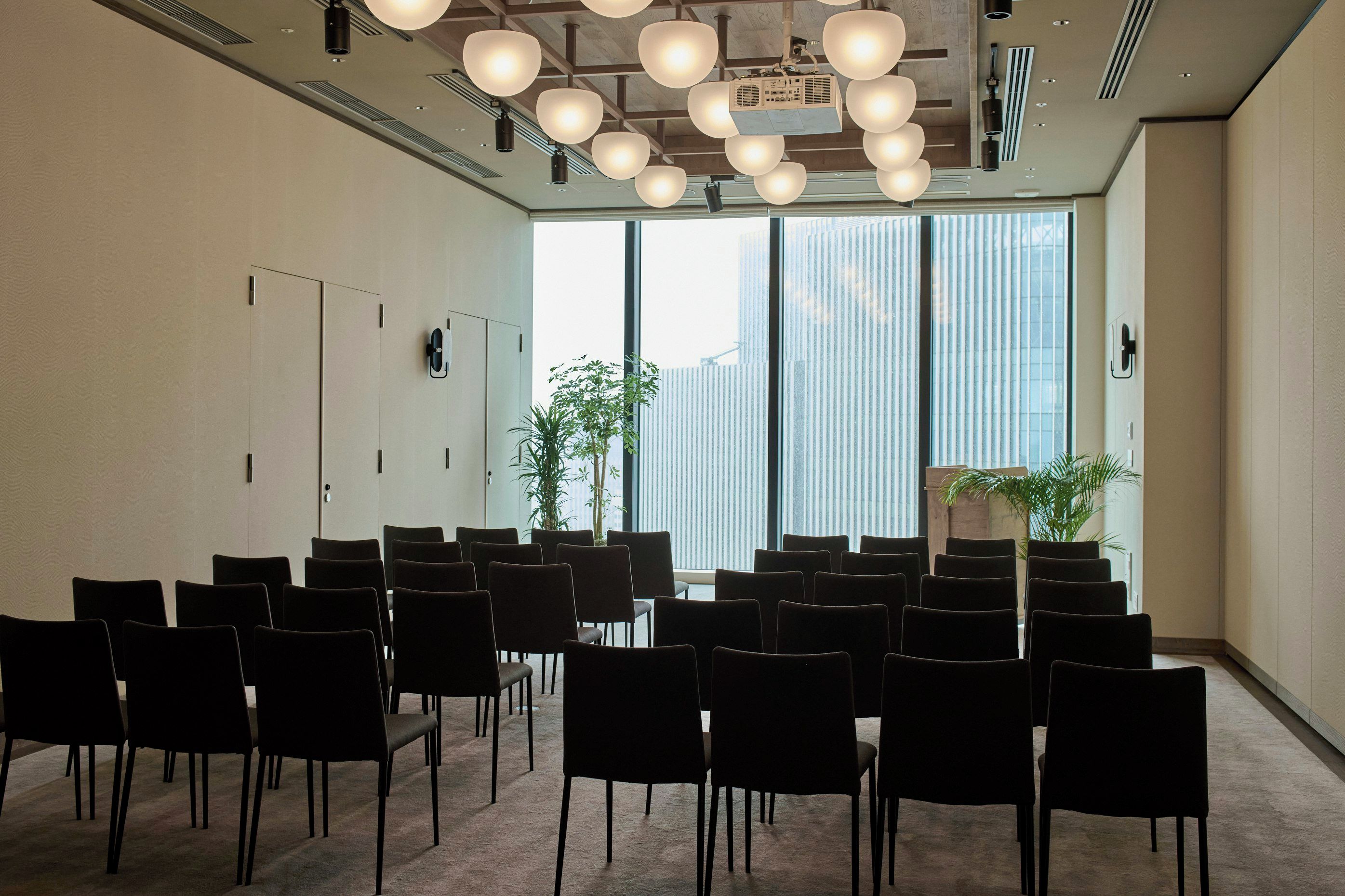 A conference room with rows of chairs, large windows, and ceiling lights.