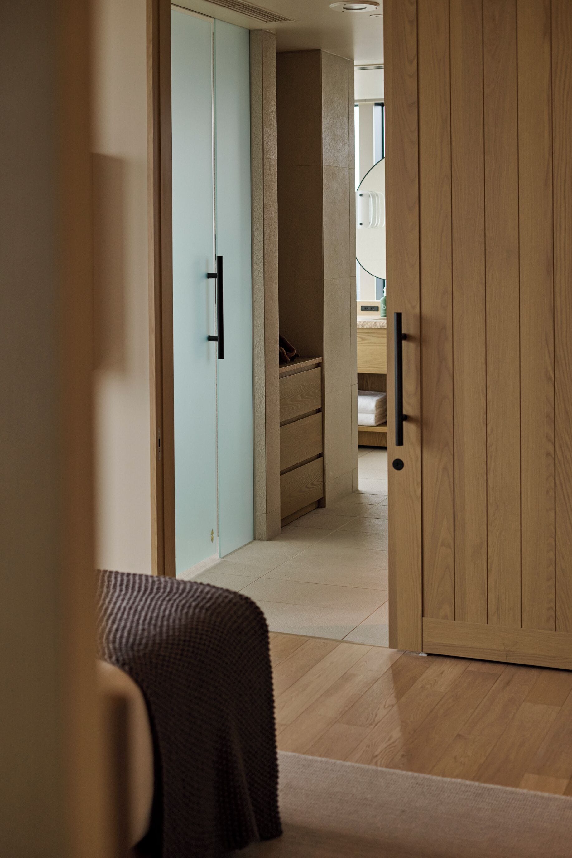 A hallway with a wooden door, a light blue wardrobe, and a bed with a brown blanket.