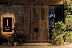 L'ingresso di un hotel con una porta in legno, una insegna che indica 'HOTEL 1 Tokyo' e piante in vaso disposte attorno all'entrata.
