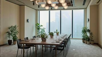 A conference room with a long table, chairs, potted plants, and a large window with a city view.