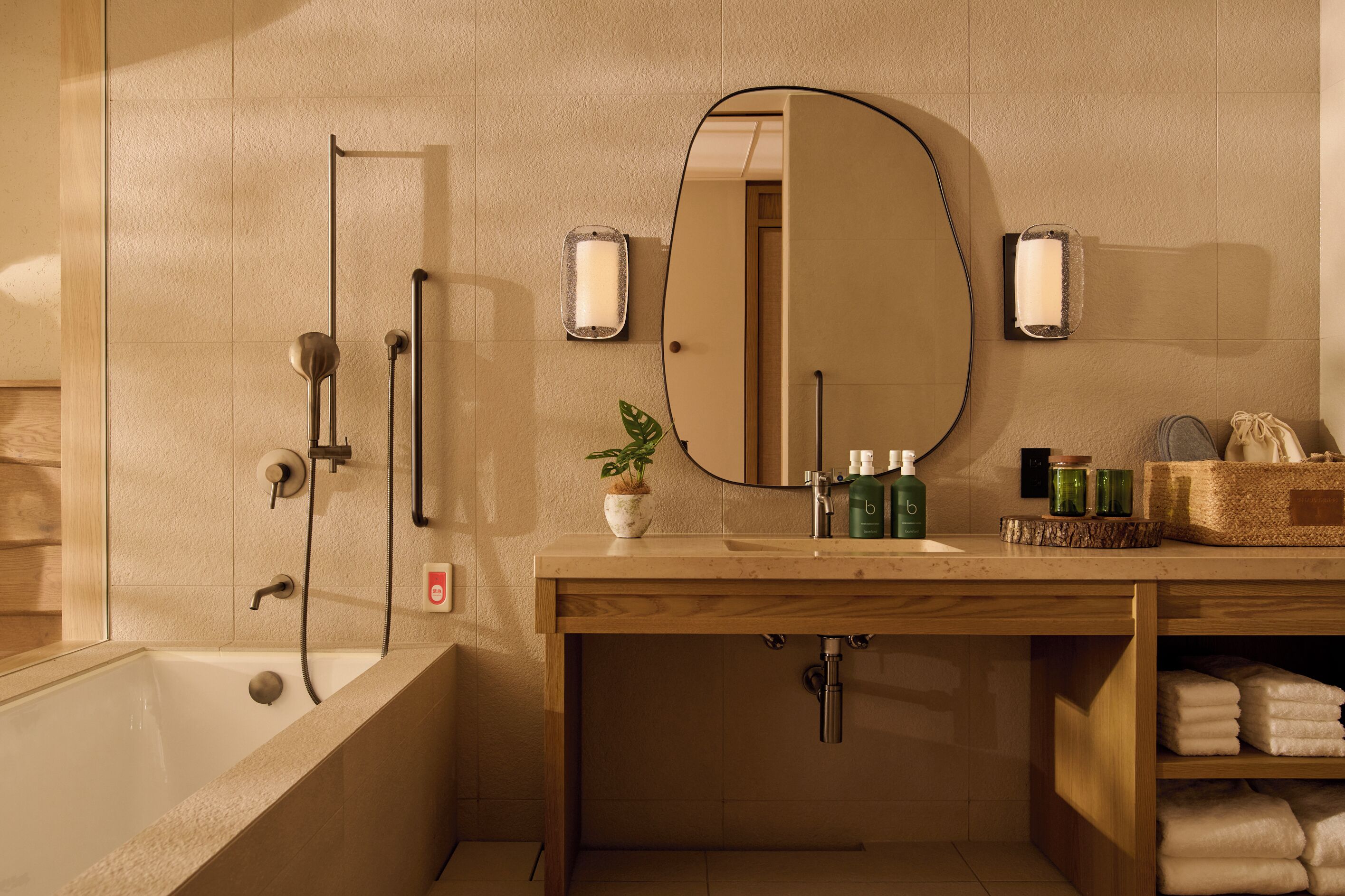 A modern bathroom with a bathtub, a mirror, and a vanity with toiletries.