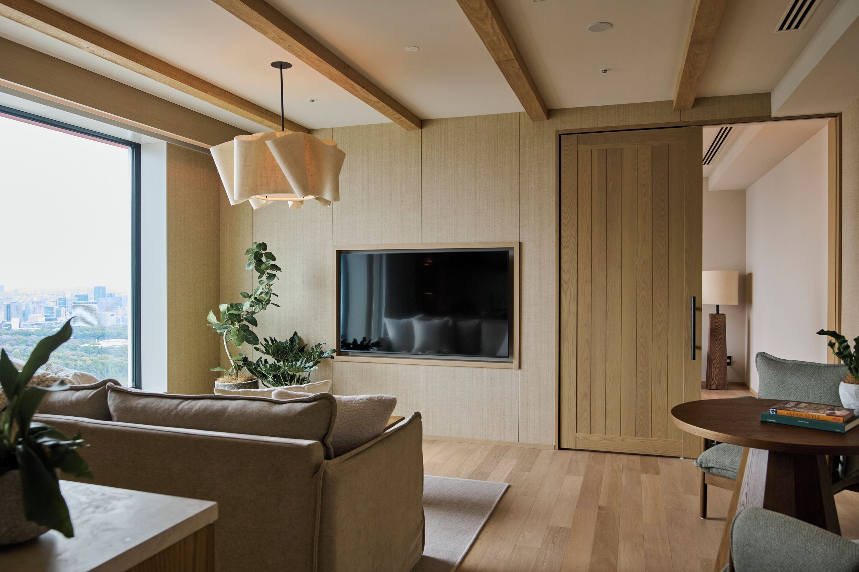 Una sala de estar moderna con un ventanal grande, un televisor de pantalla plana, un sofá, una mesa de comedor y una planta en maceta.