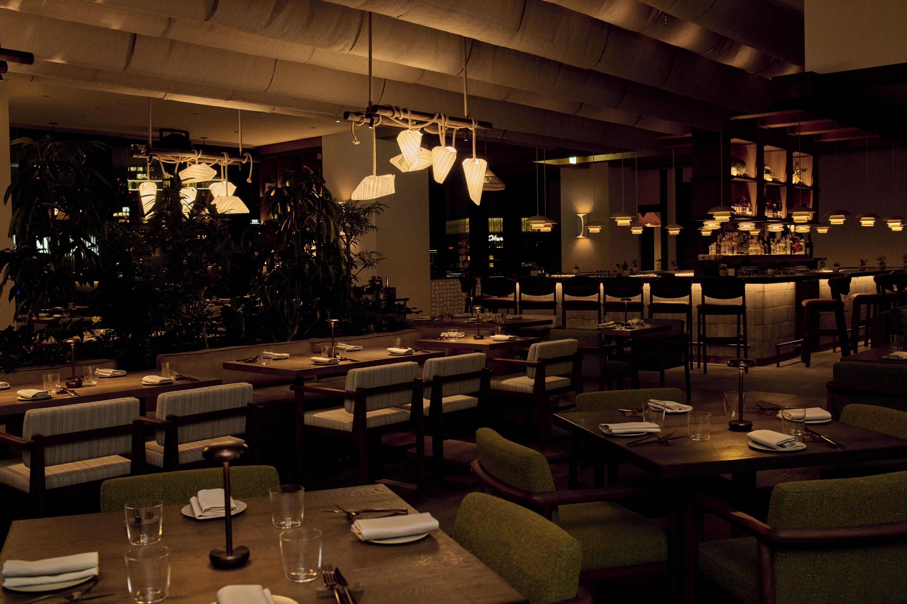 A dimly lit restaurant with multiple tables and chairs, ambient lighting, and a bar area.
