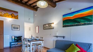 Ein gemütliches Wohnzimmer mit einem blauen Sofa, einem Esstisch mit Stühlen, einem Fernseher und Kunstwerken an den Wänden.