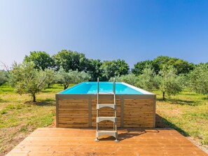 Piscina rettangolare con bordo in legno e scaletta metallica, circondata da ulivi e un cielo azzurro terso.