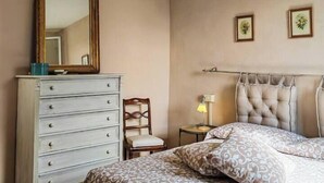 A bedroom with a bed, a dresser, a chair, a lamp, and a mirror. - View of 2 historic towers • Lucca • 2 guests (Lucca)