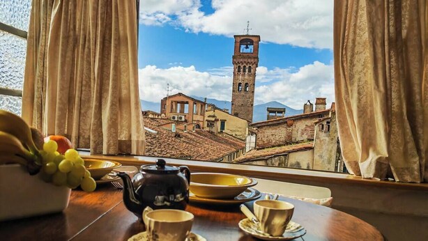 A table with a teapot, cups, and a bowl, with a view of a historic town and a tower in the background. - View of 2 historic towers • Lucca • 2 guests (Lucca)