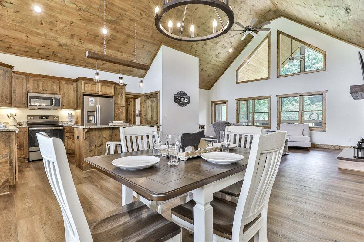 A spacious kitchen with wooden cabinets, a dining area with a table set for four, and large windows allowing natural light.
