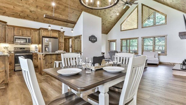 A spacious kitchen with wooden cabinets, a dining area with a table set for four, and large windows allowing natural light. - Mountaintown Chalet | Ellijay, GA (Ellijay)