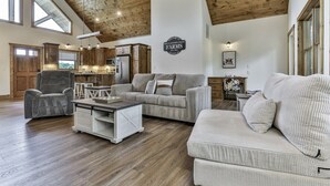 A spacious living area with a high ceiling, wooden beams, a large sofa, a dining table, and a kitchen in the background. - Mountaintown Chalet | Ellijay, GA (Ellijay)