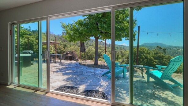 A spacious patio with a stone floor, outdoor furniture, and a view of a lush landscape with trees and hills. - 4-bedroom house in Oakhurst with views, game room, hot tub, EV charger (Oakhurst)