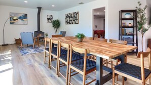 A modern living room with a wooden dining table, blue cushioned chairs, a fireplace, and a bookshelf. - 4-bedroom house in Oakhurst with views, game room, hot tub, EV charger (Oakhurst)