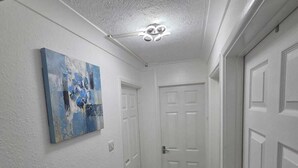 A narrow hallway with white walls, a ceiling light fixture, and a door at the end.