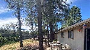 A covered outdoor patio with a table and chairs, surrounded by trees. - Ken`s Retreat- Come relax in our home (Navajo County)