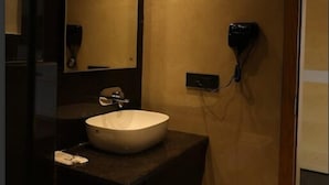 A modern bathroom with a large mirror, a round sink, and a hairdryer mounted on the wall. - Prakash Continental (Bareilly)