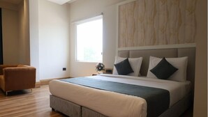 A bedroom with a large bed, a brown armchair, and a window with a view. - Prakash Continental (Bareilly)