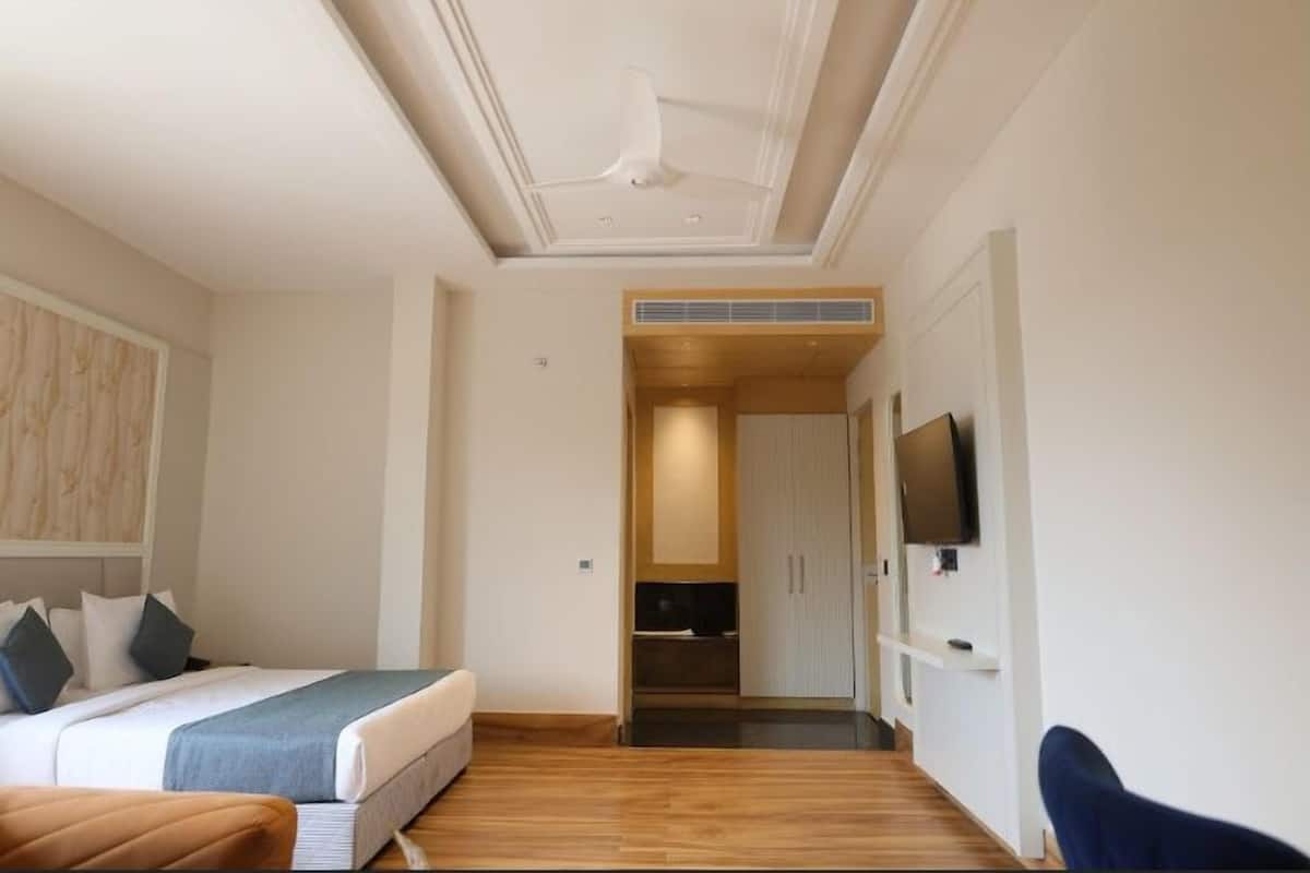 A hotel room with a bed, a desk, a chair, and a television on the wall.