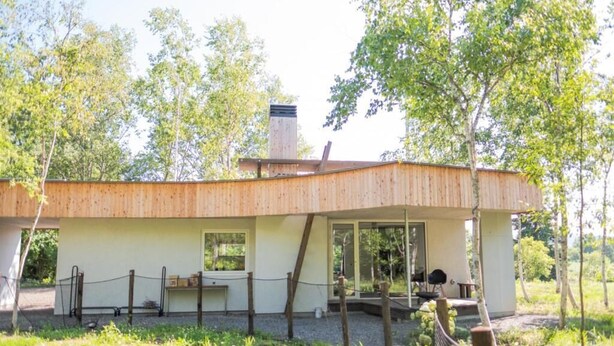 Una cabaña de madera moderna con porche cubierto, ventanas amplias y chimenea.